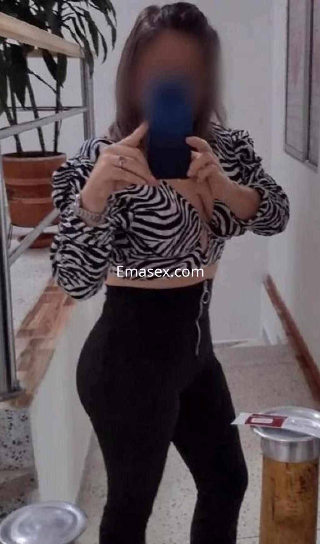 Puta en Barcelona posando frente al espejo con un top de rayas zebra y pantalones ajustados, mostrando confianza.