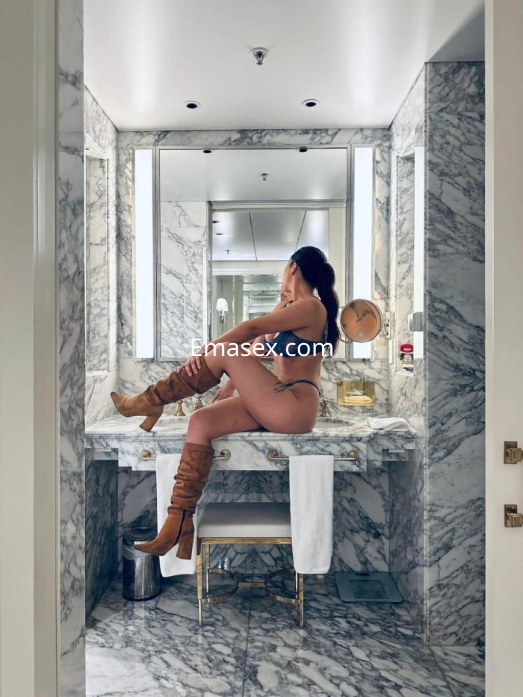 Escort en Zamora posando en un baño elegante, con lencería azul y botas largas, sentada sobre el lavabo.