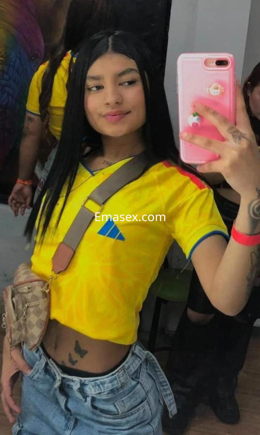 Escort en Madrid se toma una selfie con una camiseta amarilla, pantalones cortos de mezclilla y un bolso pequeño.
