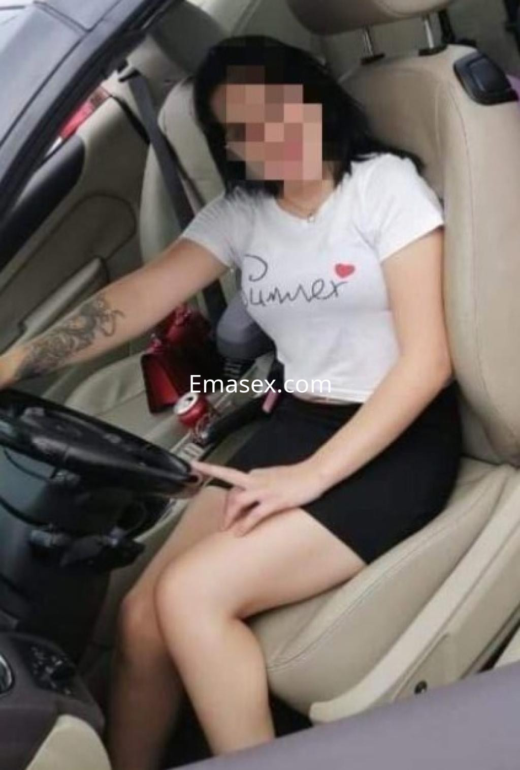 Escort en Castellón sentada en el asiento del conductor de un coche, vistiendo una camiseta blanca y falda negra.