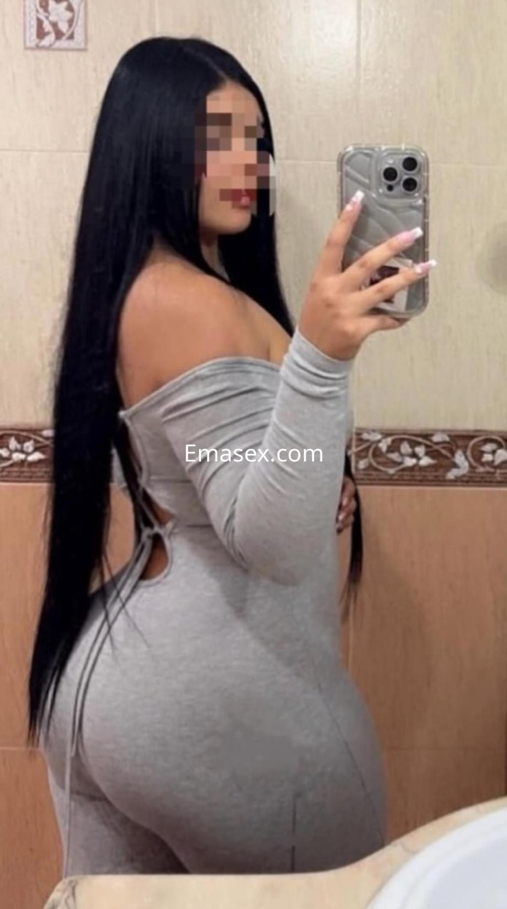La escort luce un ajustado vestido gris que resalta su figura, mientras posa en un baño en Castellón.