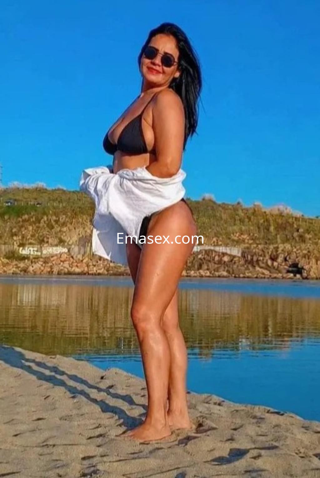 Puta en bikini negro posa en la playa de Coruña, mostrando su figura con confianza y una sonrisa.