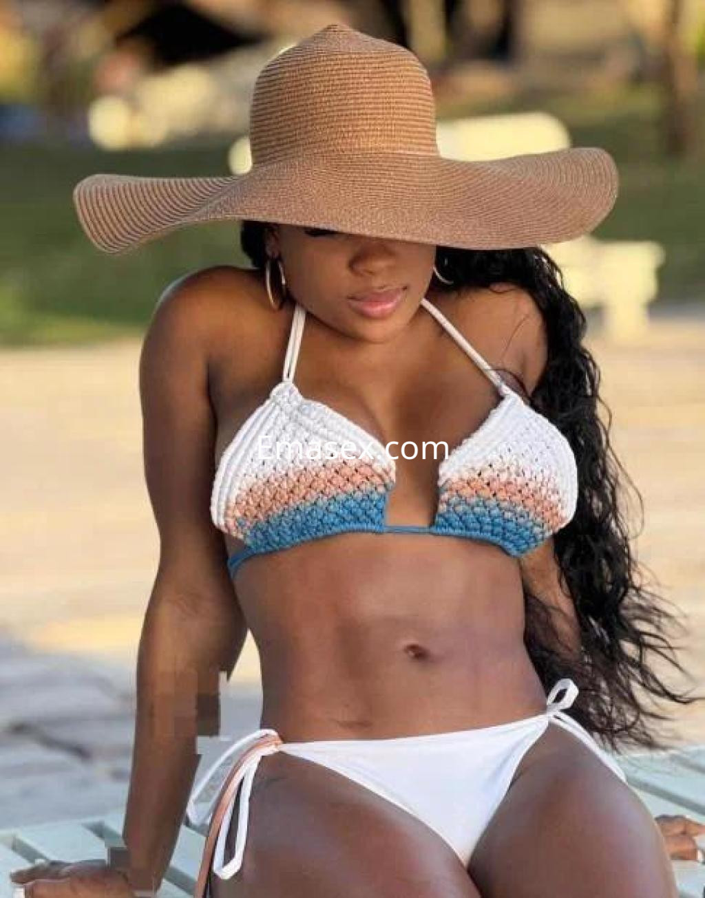 Escort en Lleida luciendo un bikini de crochet blanco y azul, con un sombrero de paja y cabello rizado.