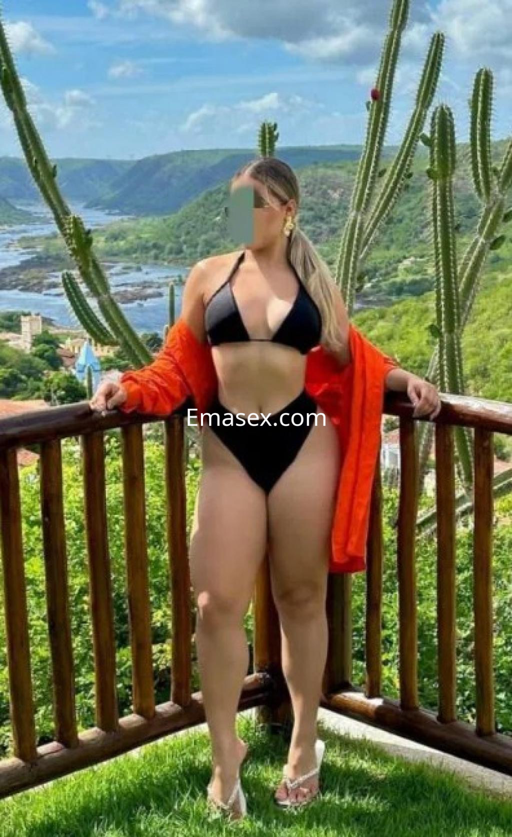 Puta en Huelva con bikini negro y chaqueta naranja, posando en un paisaje natural con cactáceas.