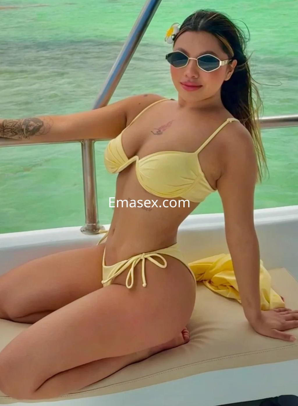 Escort en Vigo posando en un yate con un bikini amarillo, gafas de sol y un entorno marino de fondo.