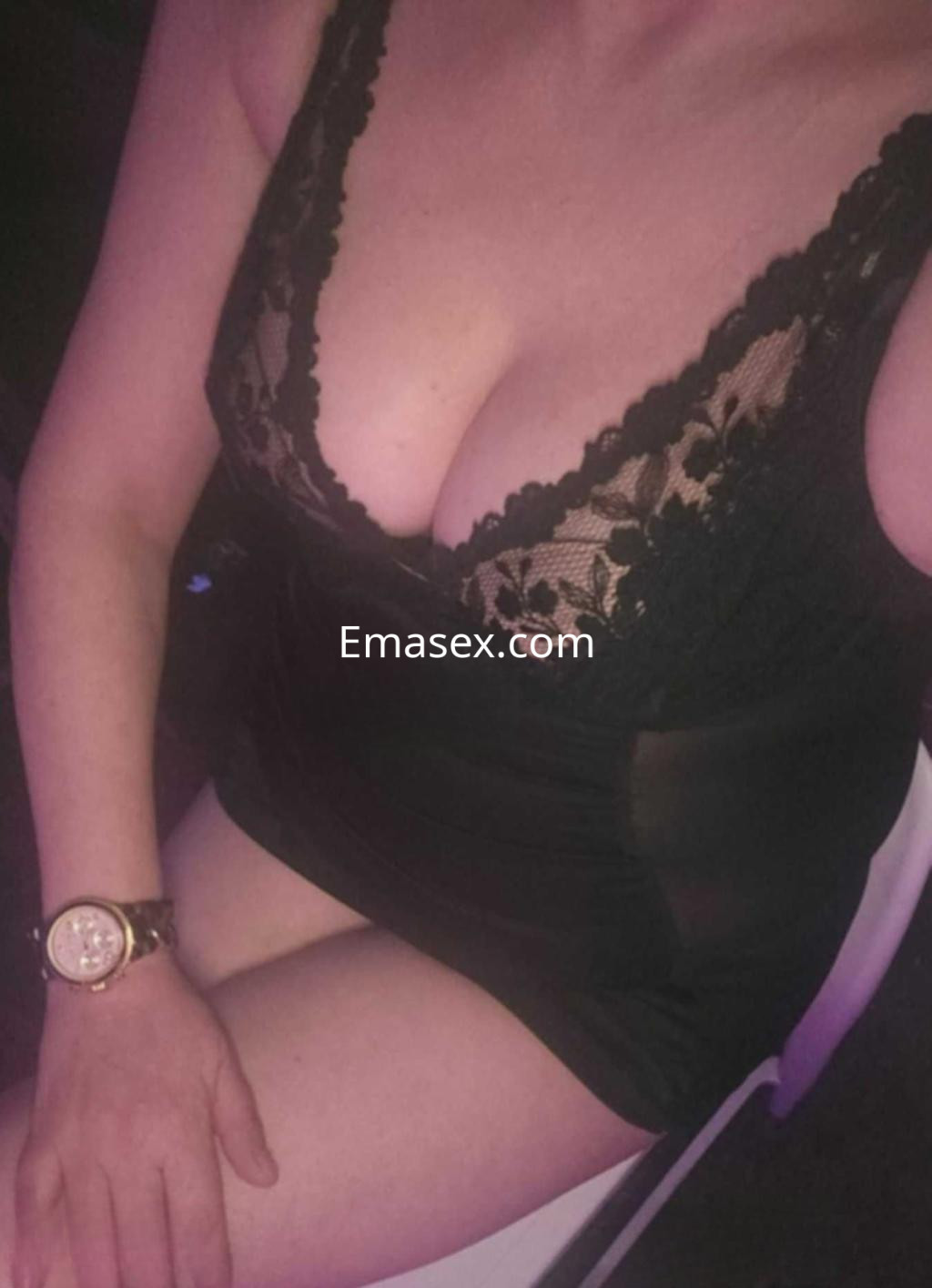 Puta en Oviedo, sentada en una silla con un vestido negro de encaje, mostrando su torso y con una pulsera en la muñeca.