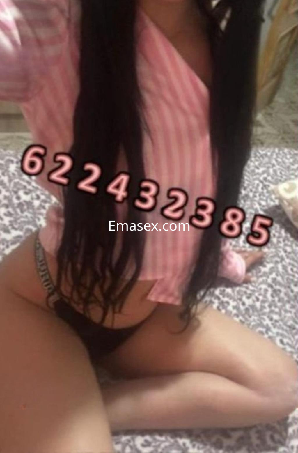Escort en Badajoz con cabello largo y oscuro, vistiendo una blusa rosa y lencería negra en un entorno acogedor.