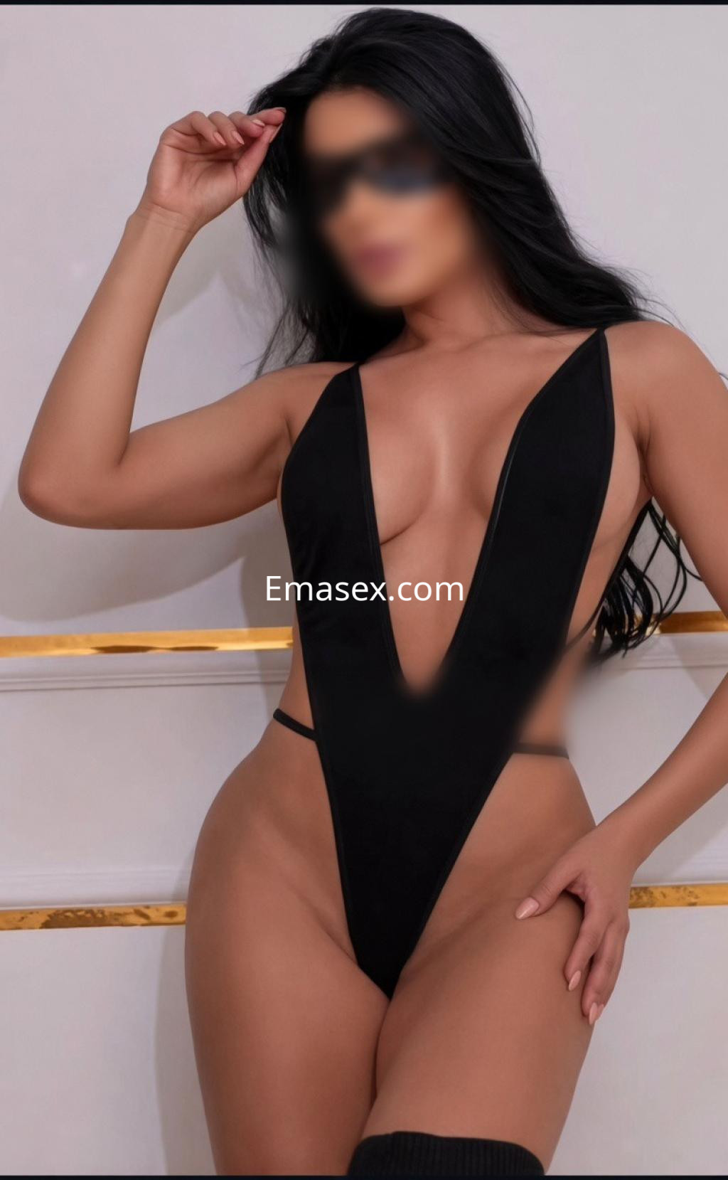 La escort en Bilbao viste un traje de baño negro de corte profundo, posando con una mano en la cabeza.