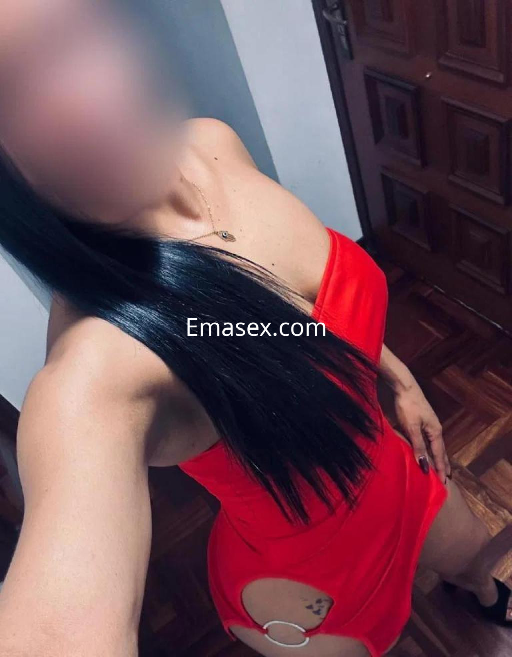 Puta con vestido rojo ajustado y detalles en la cintura, posando en un ambiente interior de Ourense.