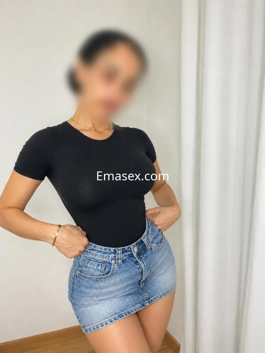 Escort en Valencia con camiseta ajustada y falda de mezclilla, posando en un entorno interior claro.