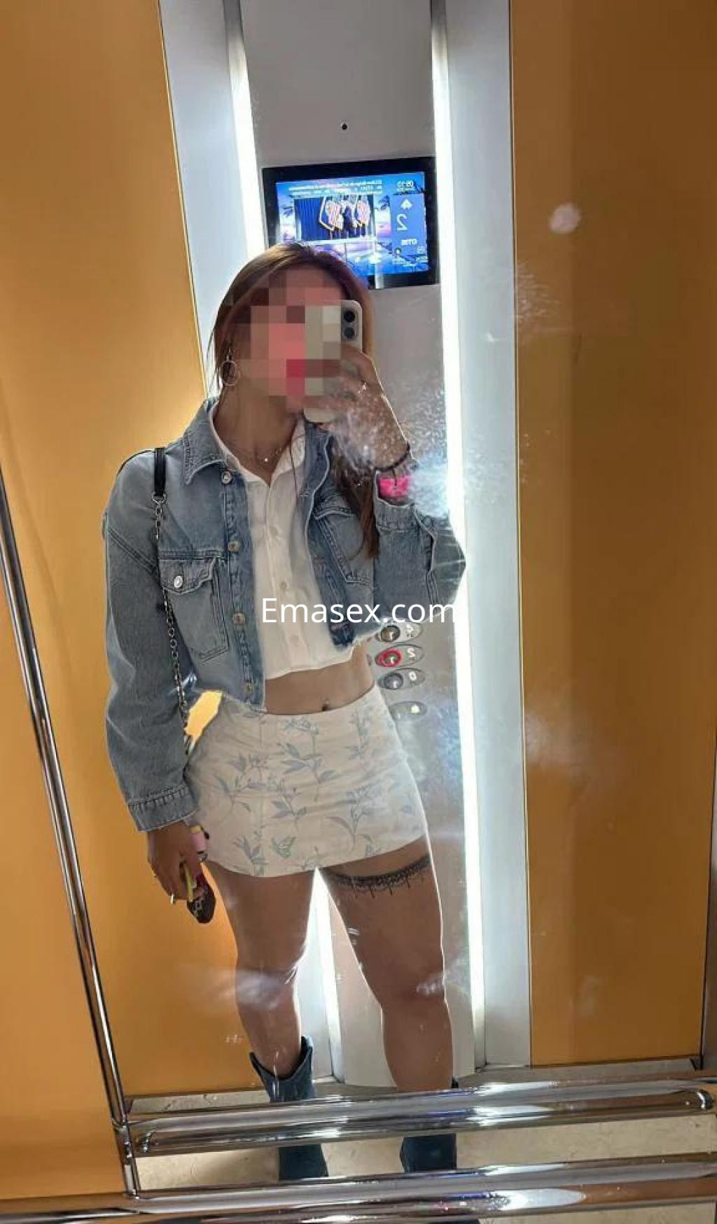 Escort en León con cabello largo y lacio, viste una blusa blanca, falda corta estampada y una chaqueta de mezclilla.