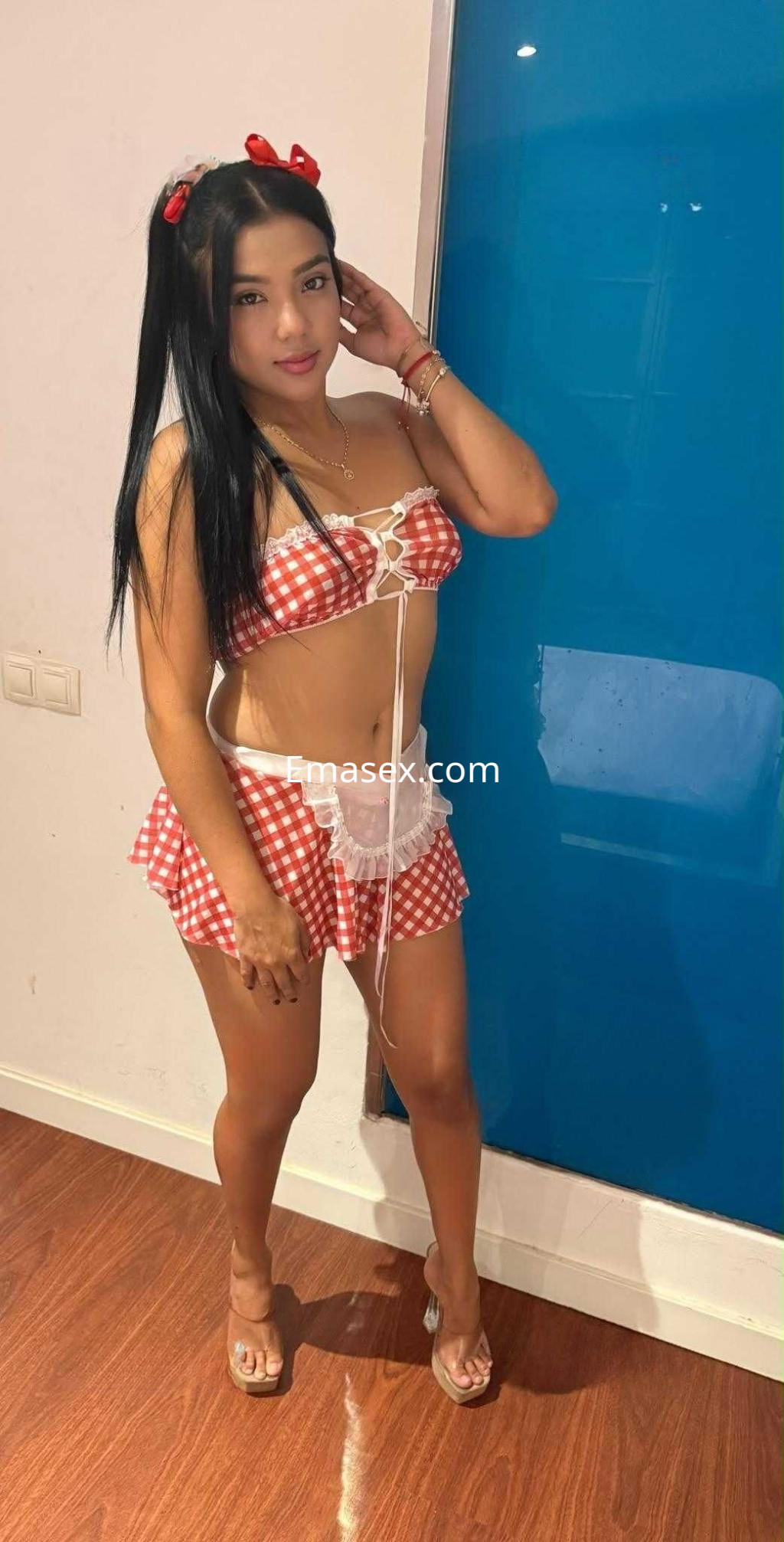 La puta en Barcelona luce un atuendo de cuadros rojos y blancos, con falda corta y sandalias, posando con una mano en la cadera.