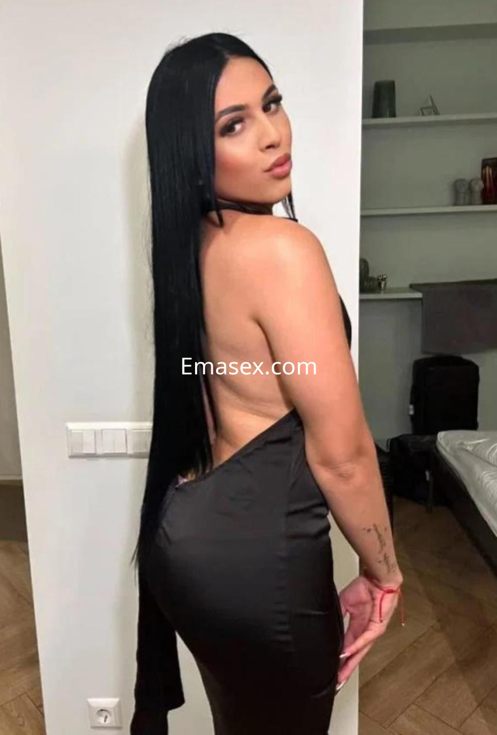 Puta en Castellón, luciendo un vestido negro sin mangas que resalta su figura, posando de perfil en un interior.