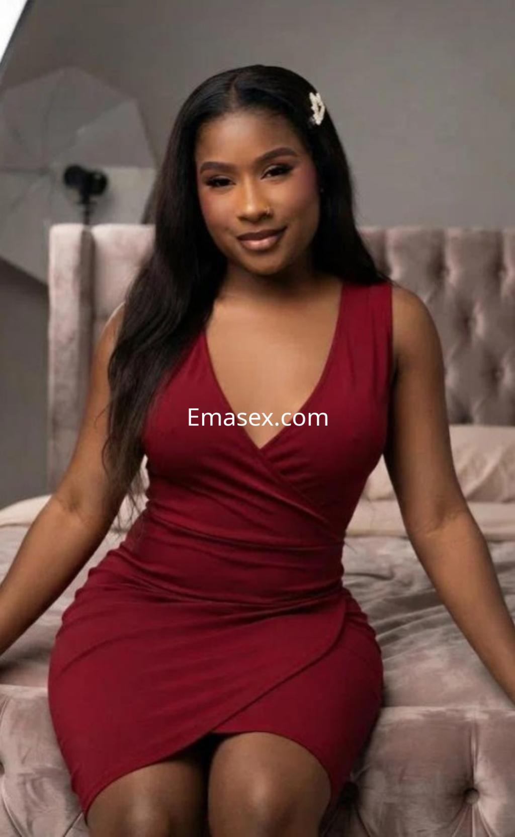 Escort en Castellón posando con un vestido rojo ajustado, sentada en un sofá con una expresión confiada.