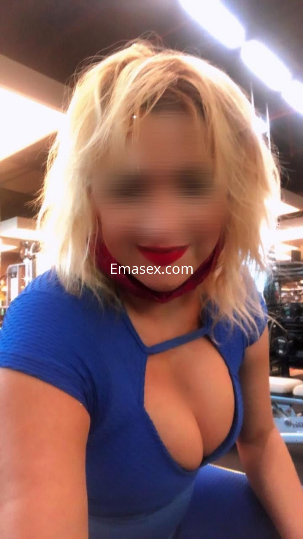 Escort en Coruña con cabello rubio y rizado, vistiendo un ajustado mono azul en un gimnasio.