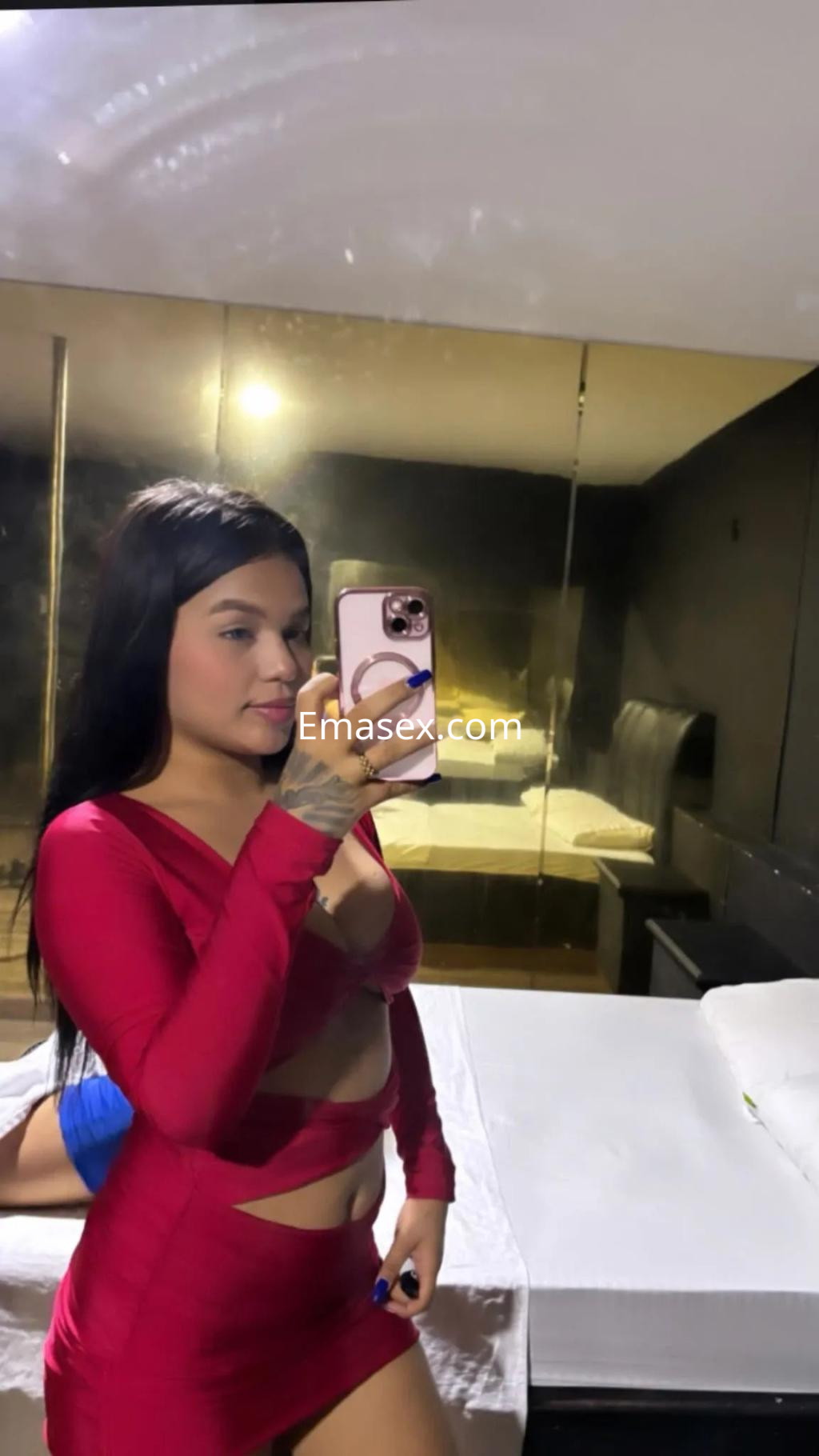 Escort en Gijón, con vestido rojo ajustado y detalles transparentes, posando frente a un espejo en un ambiente interior.