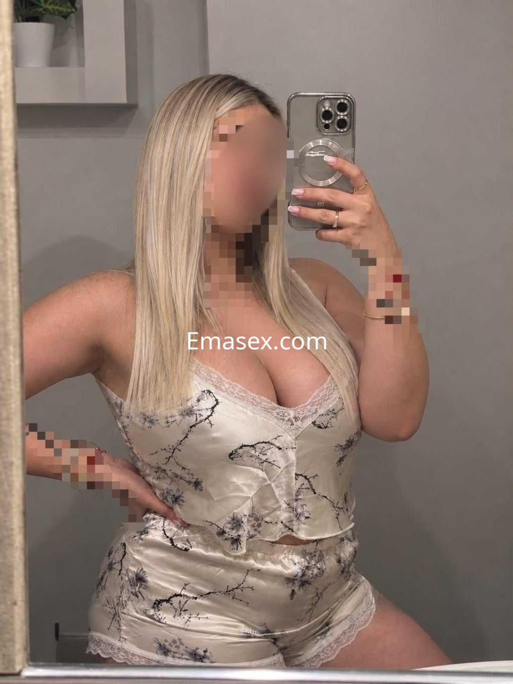 Escort en Madrid luciendo un conjunto de seda claro con estampado floral y cabello rubio, posando frente al espejo.