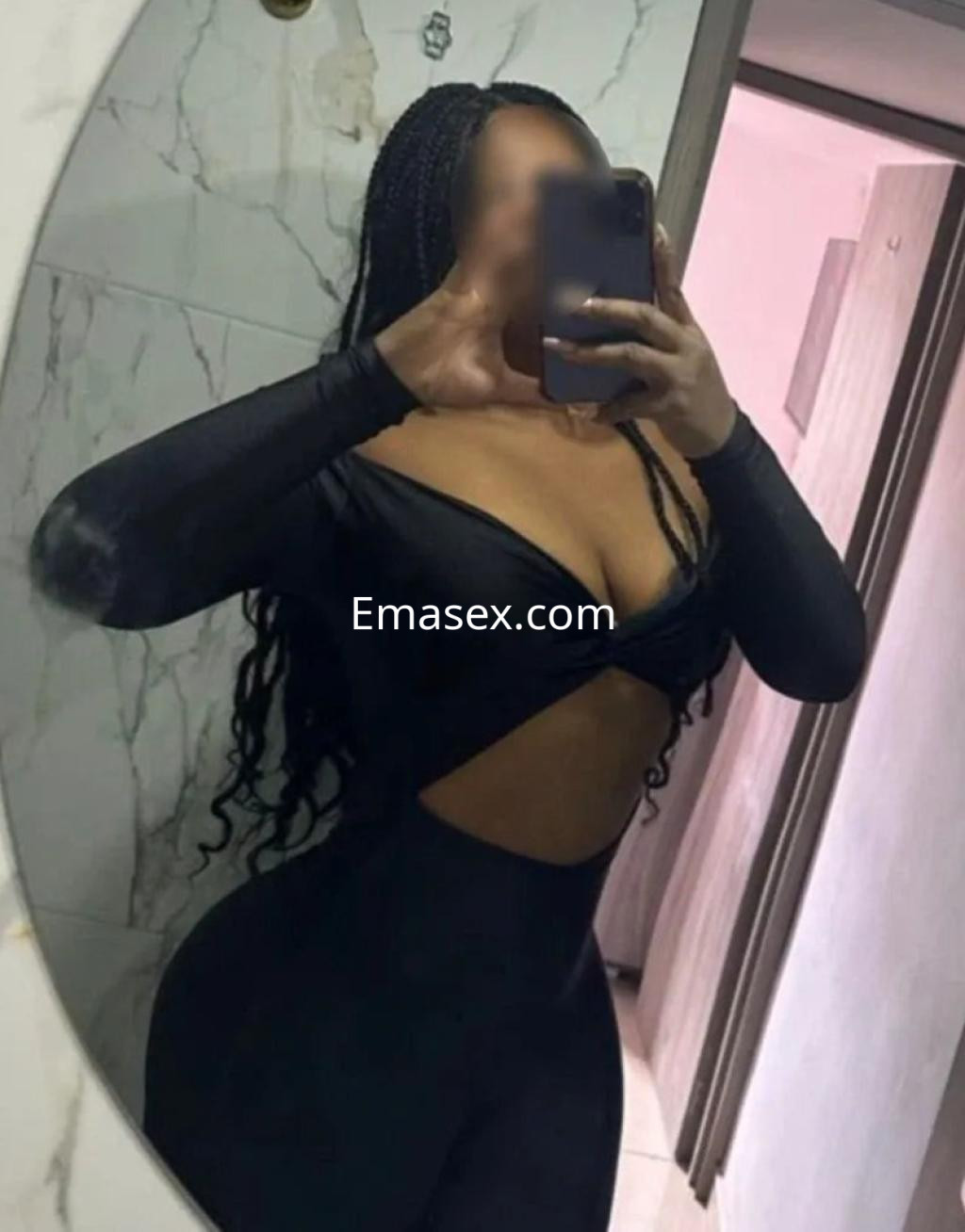 Puta en Alicante con cabello trenzado, vistiendo un body negro ajustado mientras se toma una selfie frente al espejo.