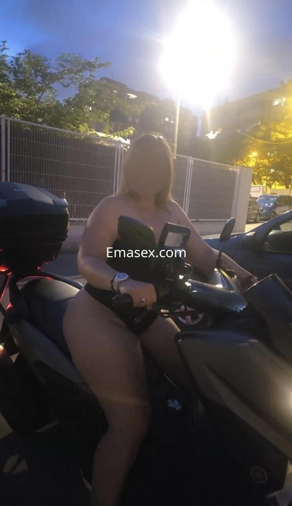 Escort posando sobre una motocicleta en Barcelona, con un atuendo de lencería negro y un ambiente nocturno.
