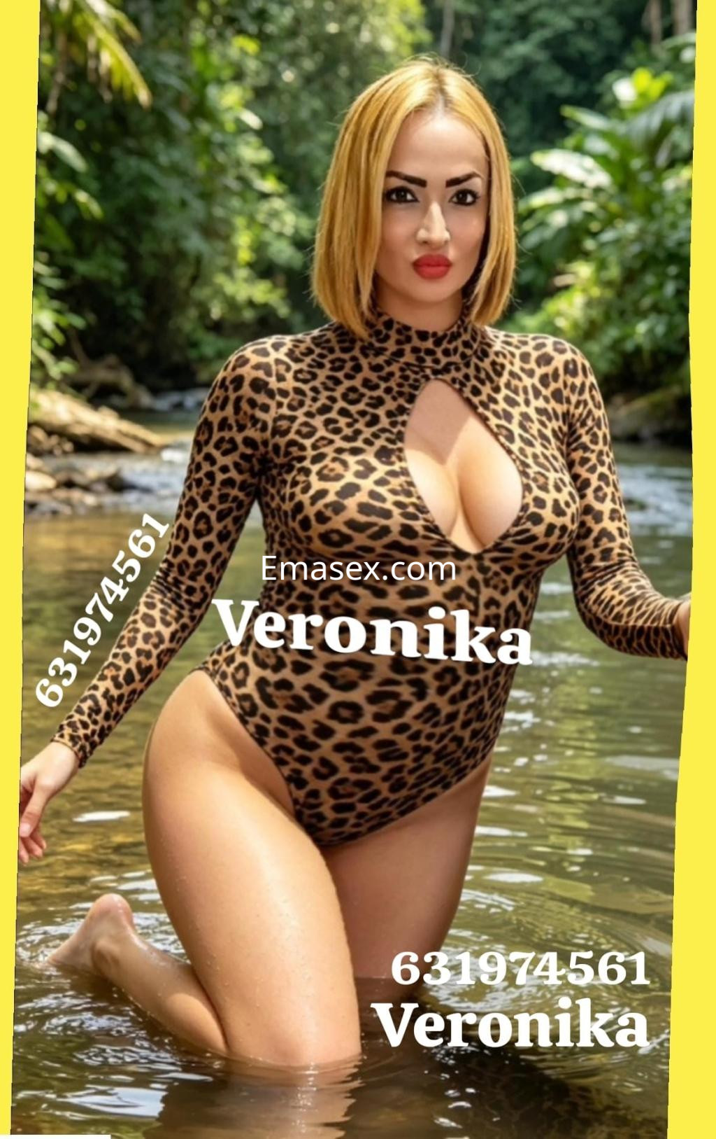 Escort en Ibiza con cabello rubio corto, vistiendo un traje de baño de leopardo, posando en el agua rodeada de vegetación.