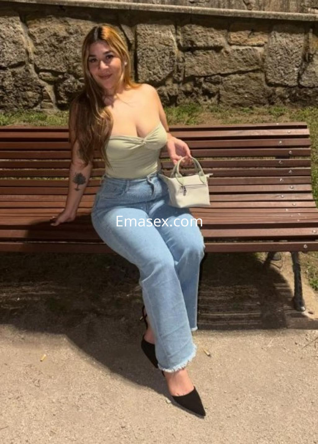 Puta sentada en un banco, con blusa sin mangas y jeans ajustados, en un entorno urbano de Ourense.