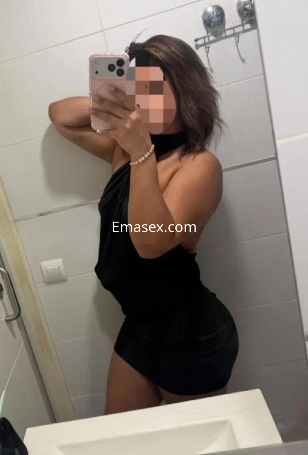 La puta en Ourense se muestra posando en un baño, luciendo un vestido negro ajustado y cabello suelto.