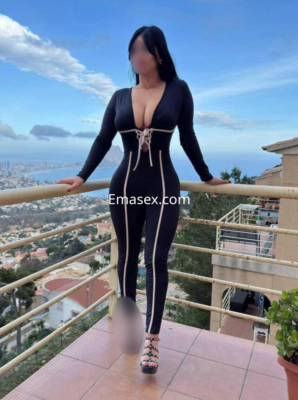 Escort en Vigo con un mono negro ajustado que destaca su figura, posando con vista panorámica al fondo.