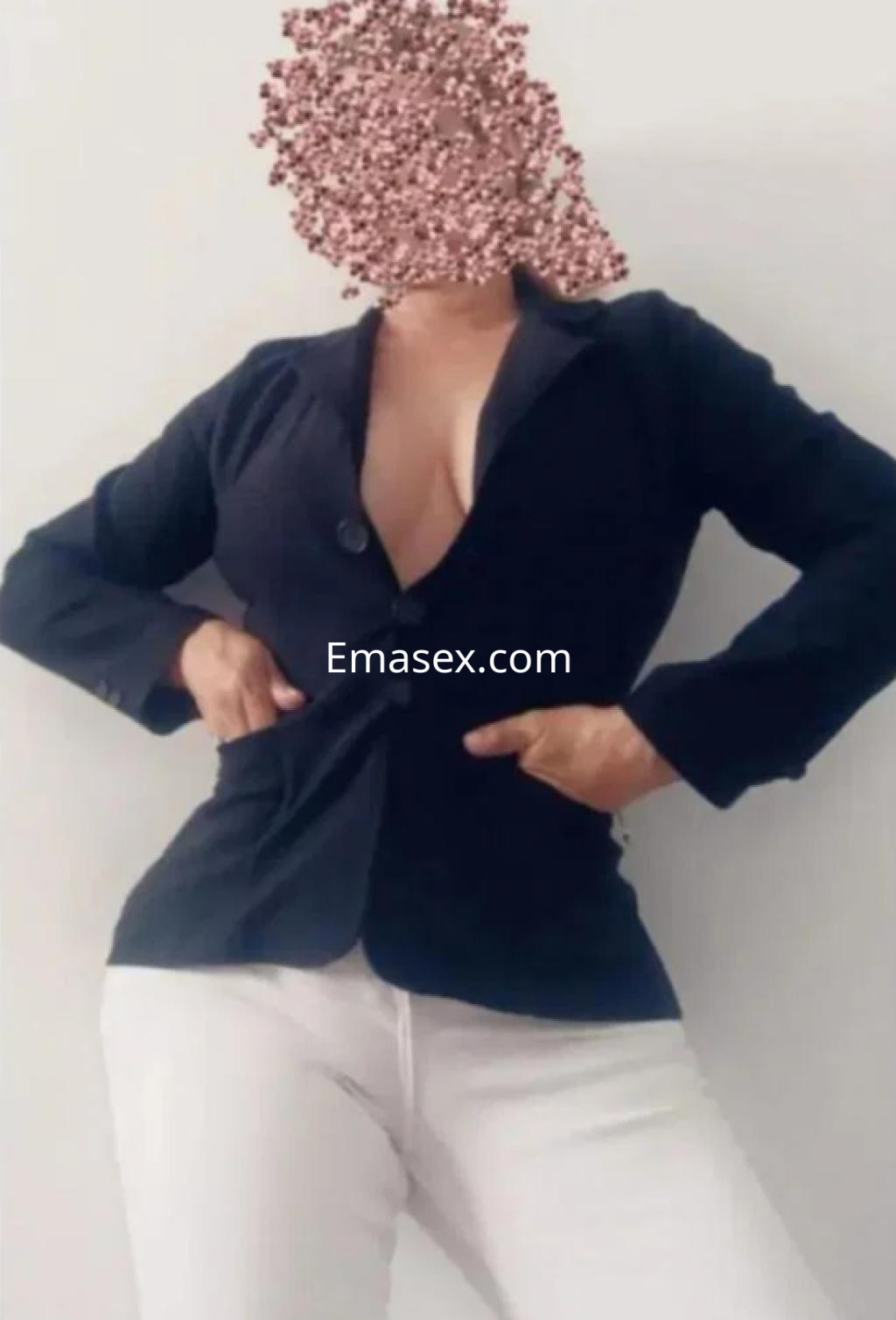 Puta en Pamplona viste un chaleco negro ajustado y pantalones blancos, mostrando una pose segura y seductora.