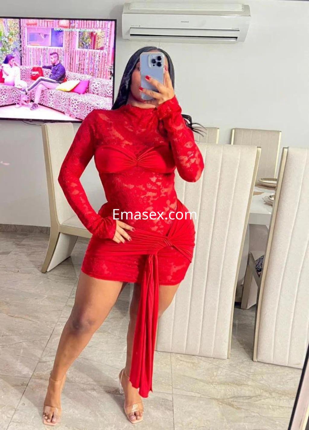 La puta viste un ceñido vestido rojo con encaje, posando en un moderno salón en Palma de Mallorca.