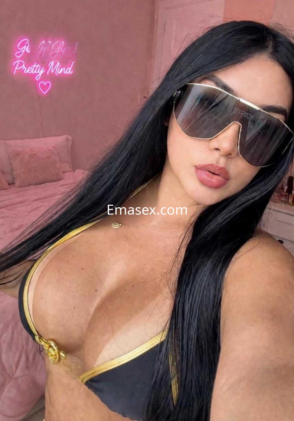 Escort en Ibiza con cabello largo y negro, usando un bikini negro con detalles dorados y gafas de sol grandes.