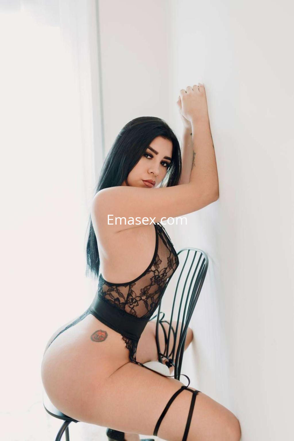 Escort posando sobre una silla negra, vistiendo un conjunto de lencería negra con encaje en Ibiza.