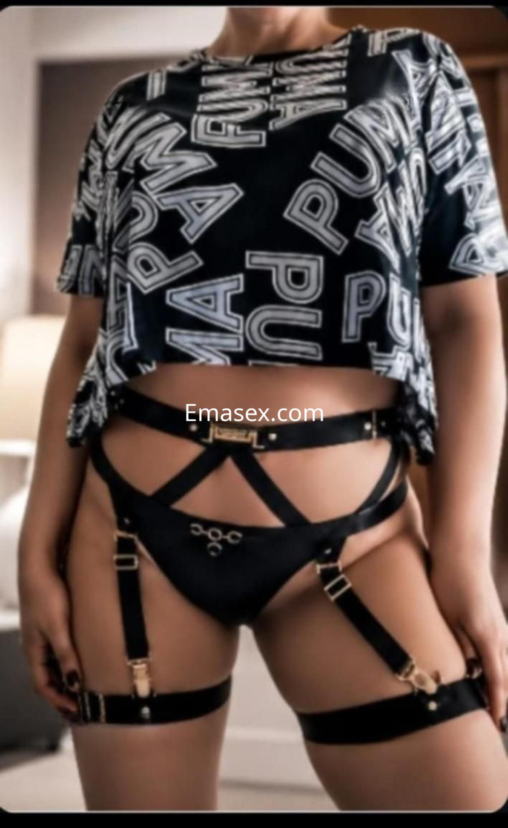 Escort en Granada, vistiendo un conjunto de ropa interior negra con tirantes, posando de frente en un ambiente moderno.