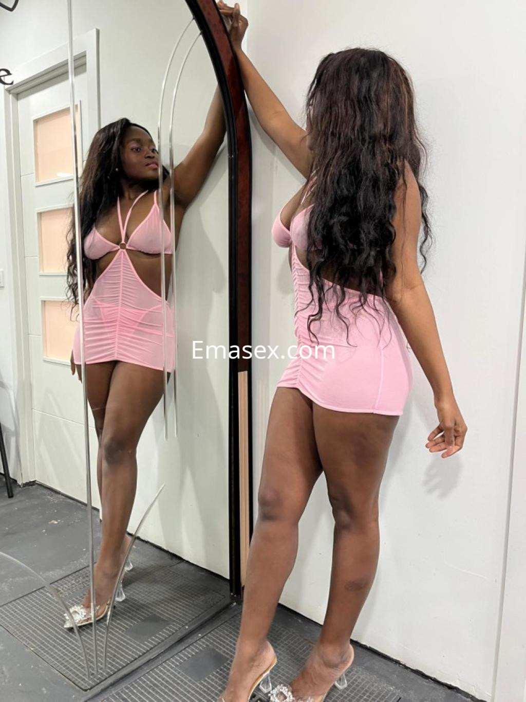 La puta viste un vestido rosa ajustado y transparente, posando frente a un espejo en León.