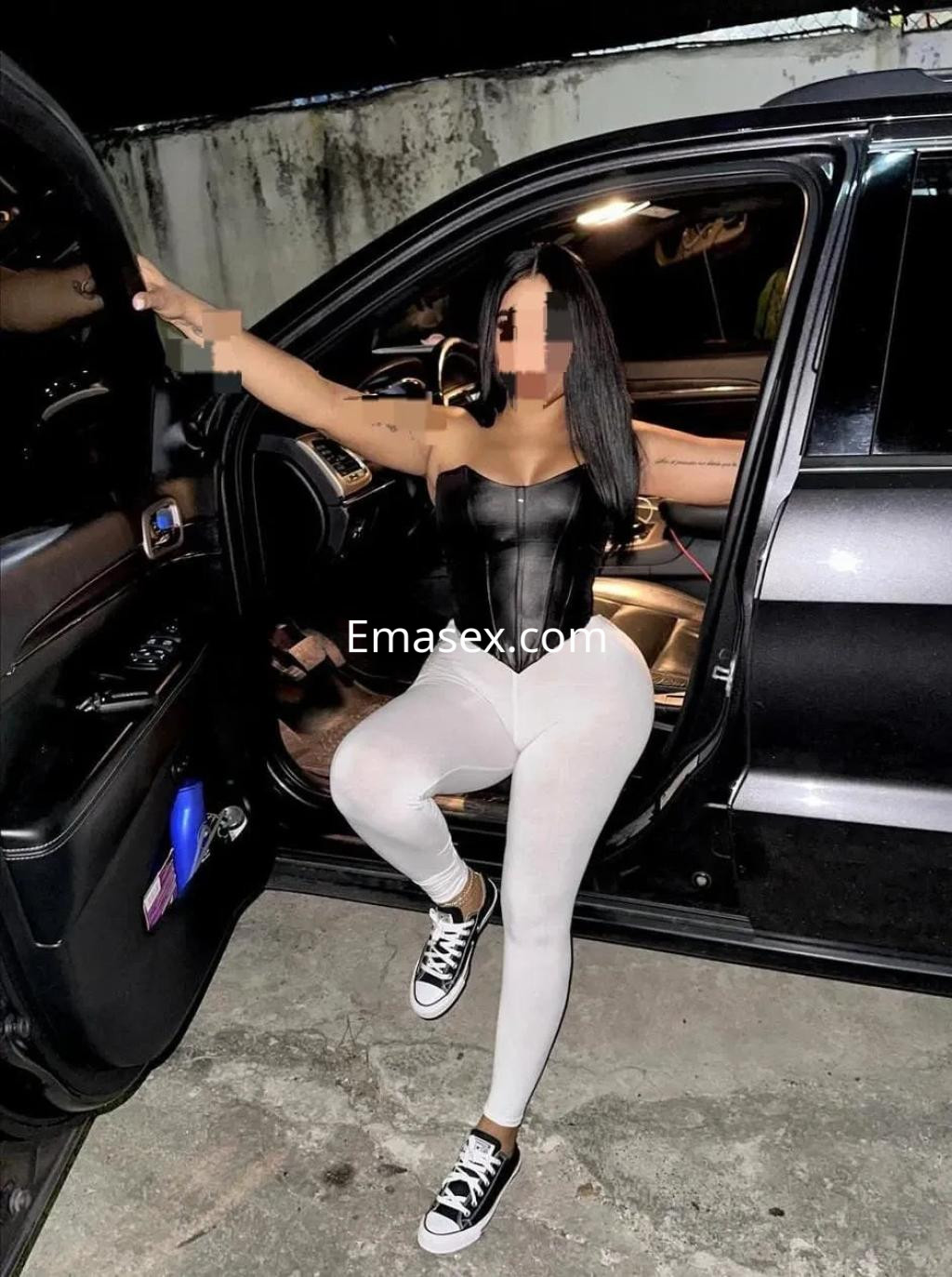 Escort en Valladolid con un ajustado corset negro y leggins blancos, sentada en el asiento del coche.