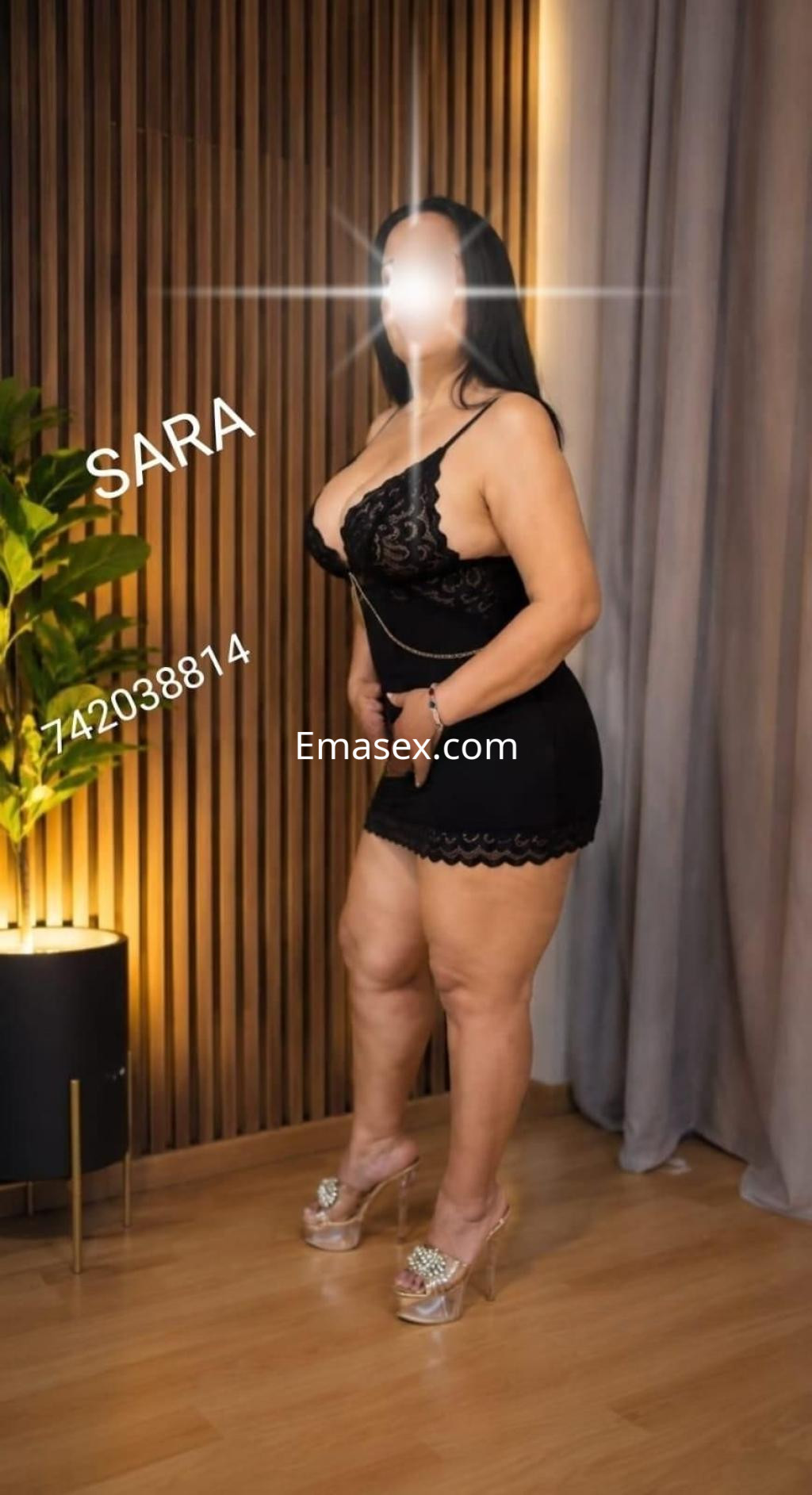 La puta viste un vestido negro ajustado y tacones transparentes, posando en un entorno moderno en Zamora.
