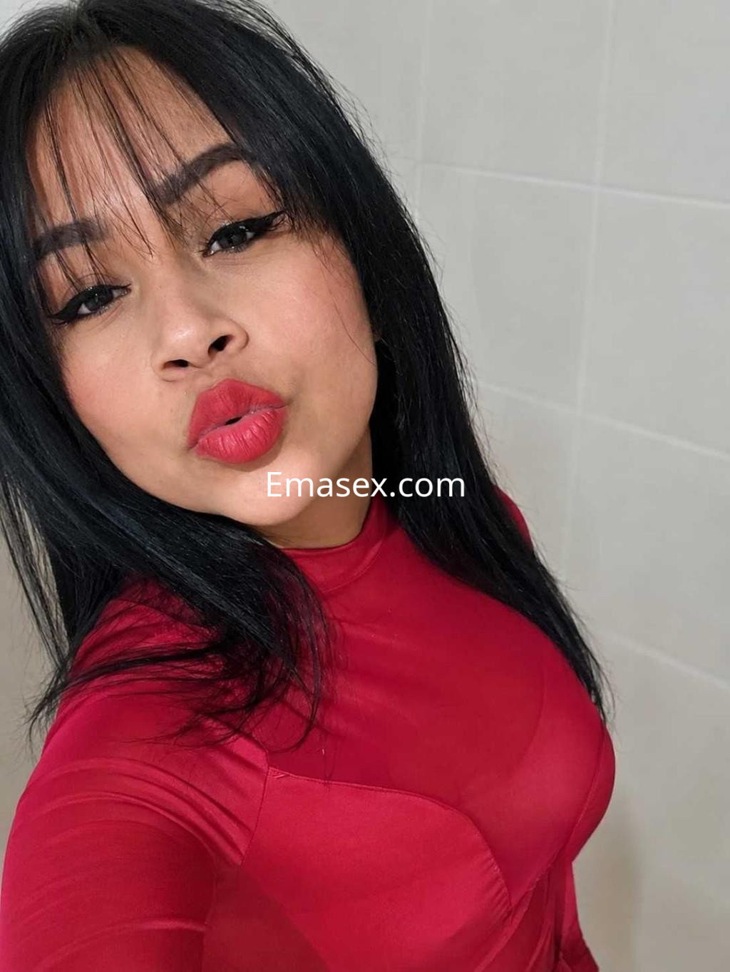 Escort en Pontevedra con cabello negro y lacio, viste un ajustado vestido rojo y labios rojos, sonriente.