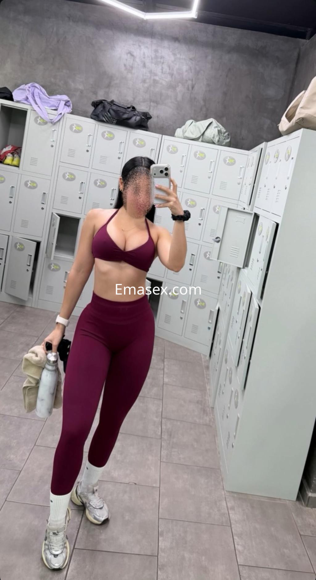 Puta en Santiago posando en un gimnasio, con top deportivo morado y leggings ajustados, sosteniendo una botella.