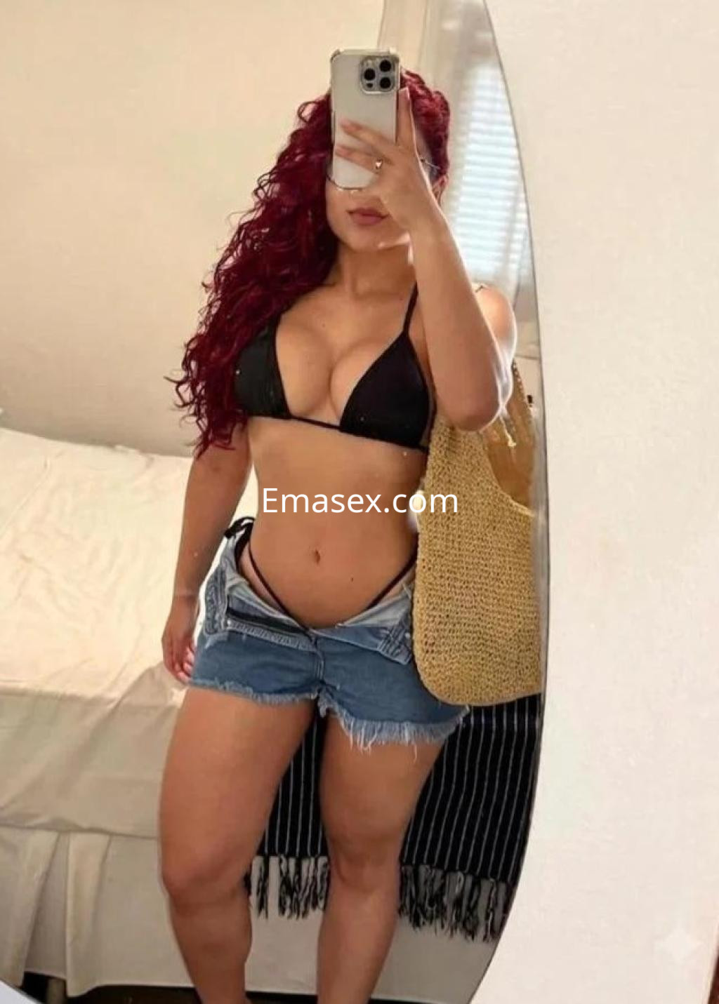 Puta con cabello rizado y rojo, luciendo un bikini negro y shorts de mezclilla en un entorno interior en Alicante.