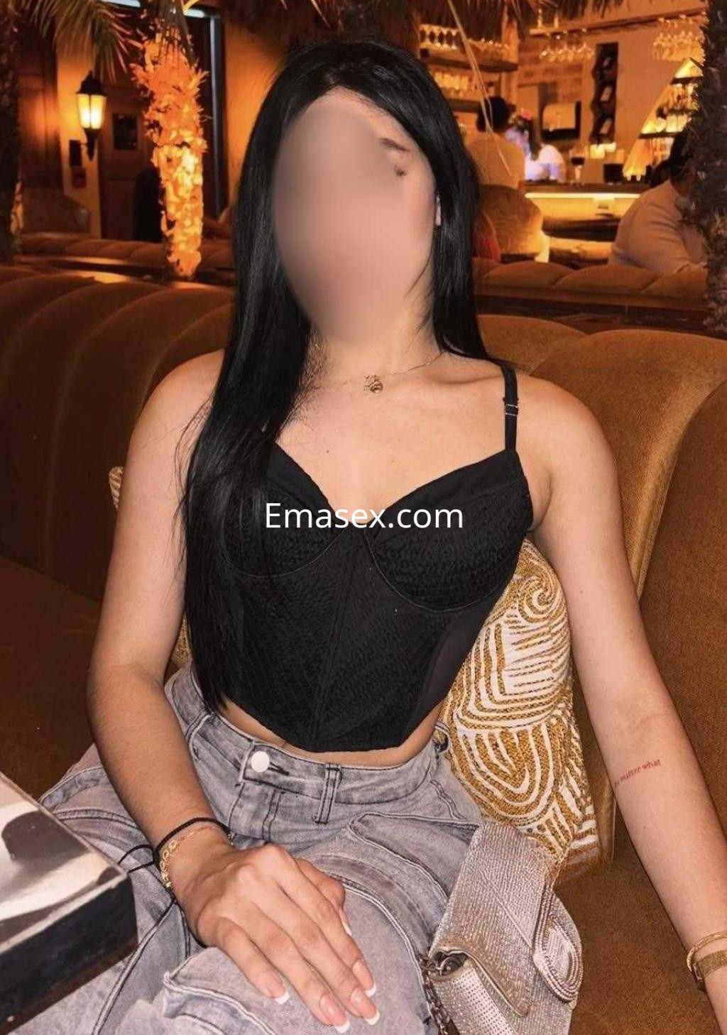 Puta en Alicante, con cabello largo y lacio, viste un top negro ajustado y jeans claros, sentada en un sofá.