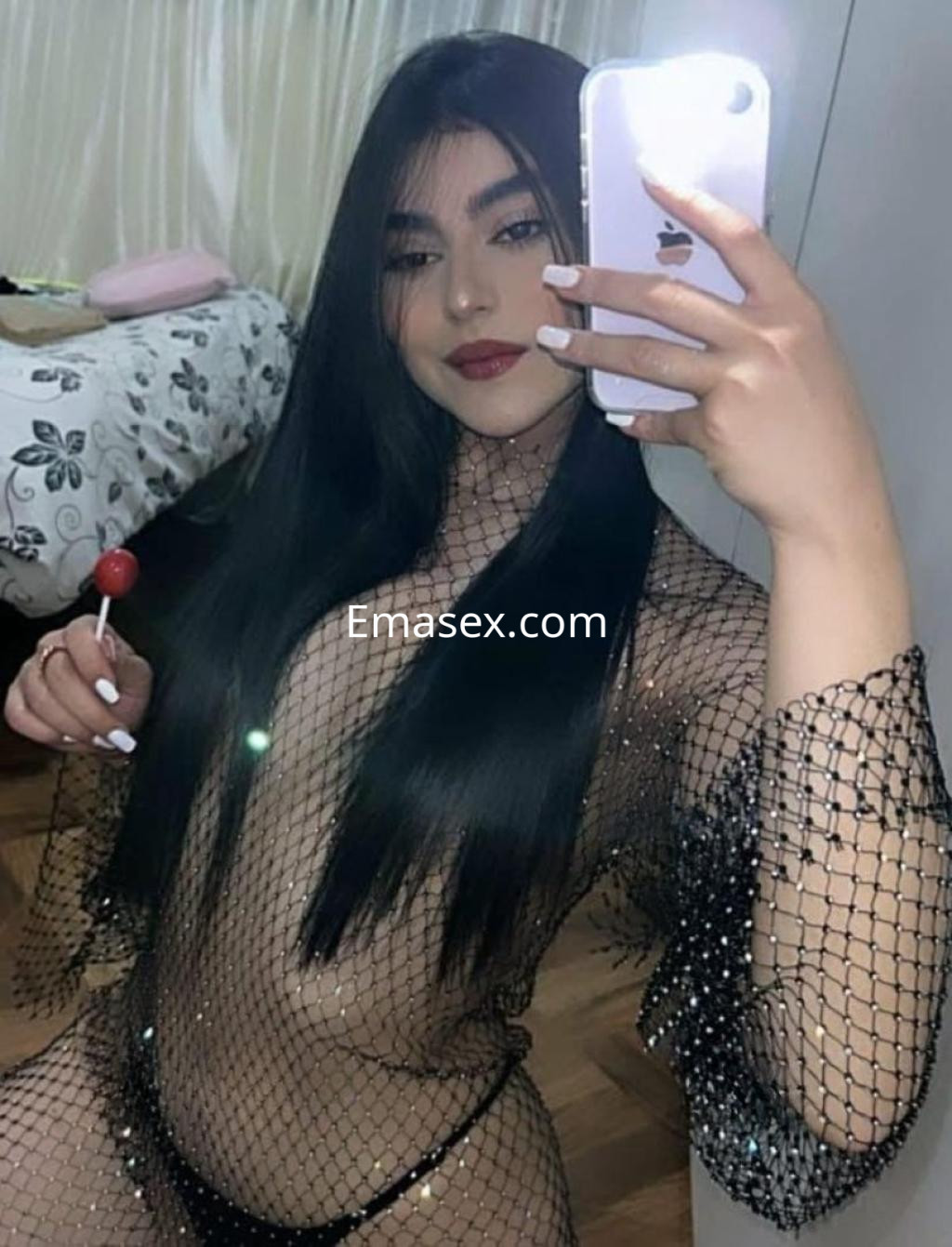 Escort de cabello largo y lacio, viste una malla transparente y sostiene un caramelo mientras posa en Alicante.