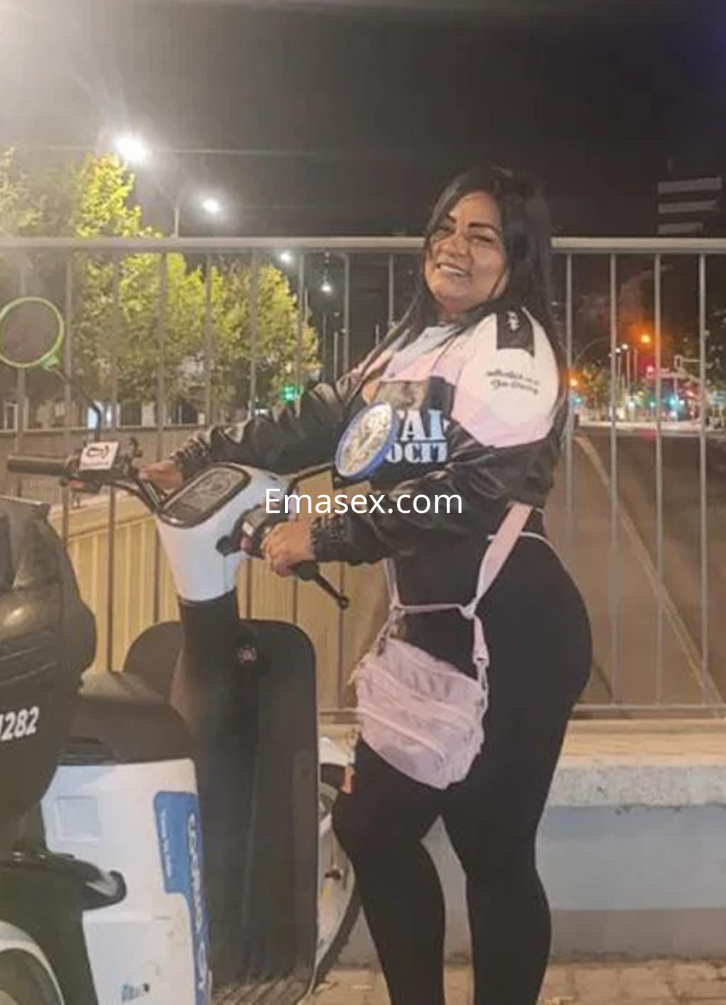 La puta se apoya en un scooter eléctrico, luciendo una chaqueta negra y un bolso rosa en Logroño.
