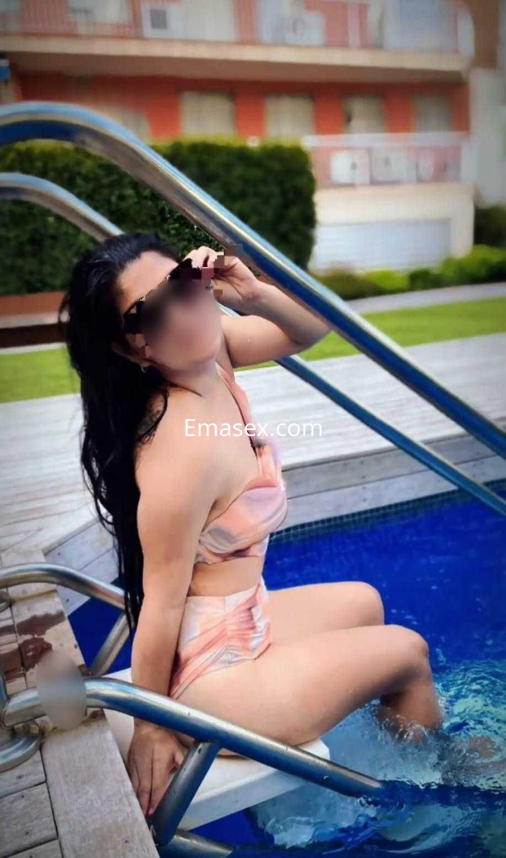 Puta de Tenerife sentada en el borde de una piscina, con un bikini de tonos suaves y gafas de sol.