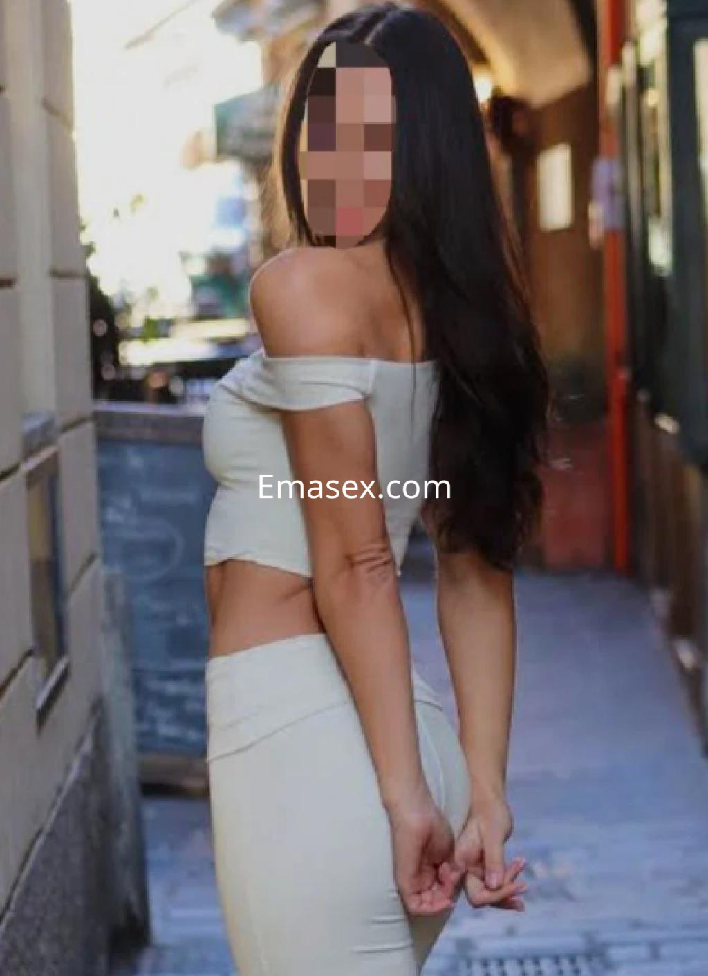 Escort en Santander con un top ajustado de tirantes y una falda larga, posando de espaldas en una calle.