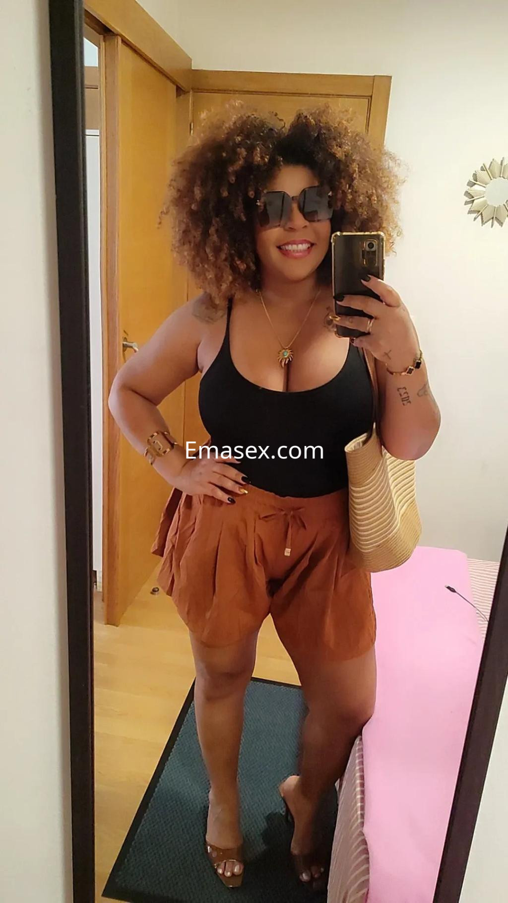 Puta con cabello rizado y oscuro, viste blusa negra y pantalones cortos marrones en un ambiente interior en Madrid.