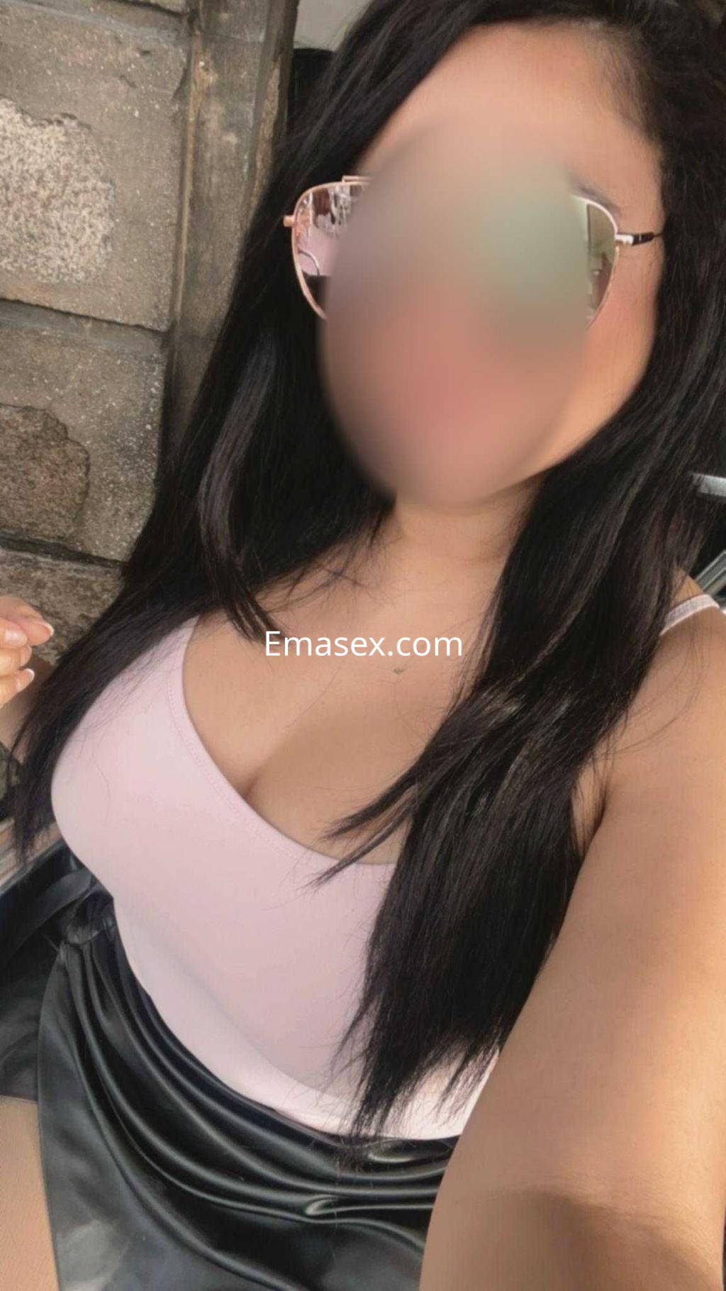 Escort en Madrid con cabello largo y oscuro, usando una blusa rosa y una falda negra, luciendo gafas de sol.
