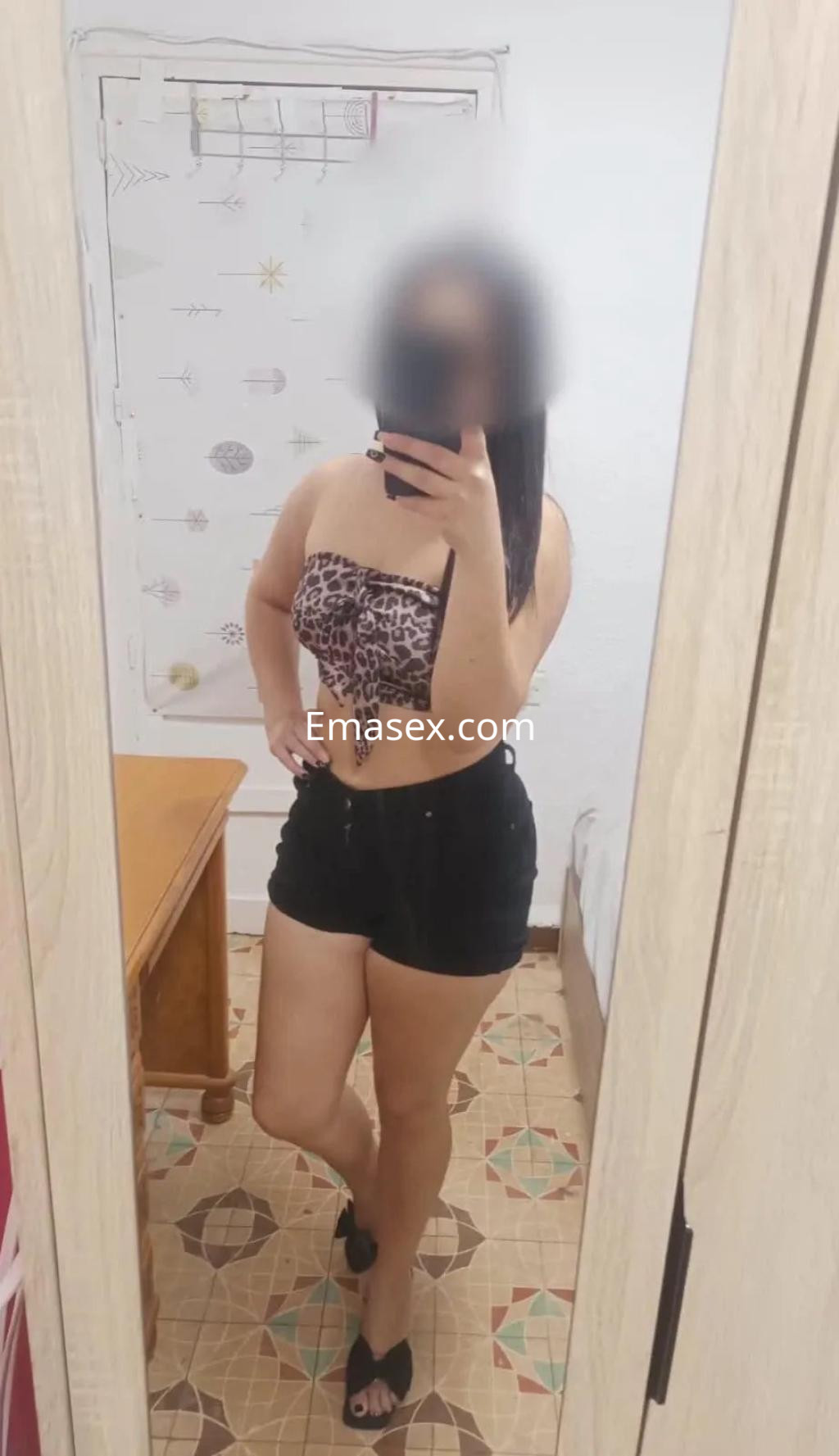 Puta en Albacete posando frente al espejo con blusa de leopardo y shorts negros, luciendo un look casual.