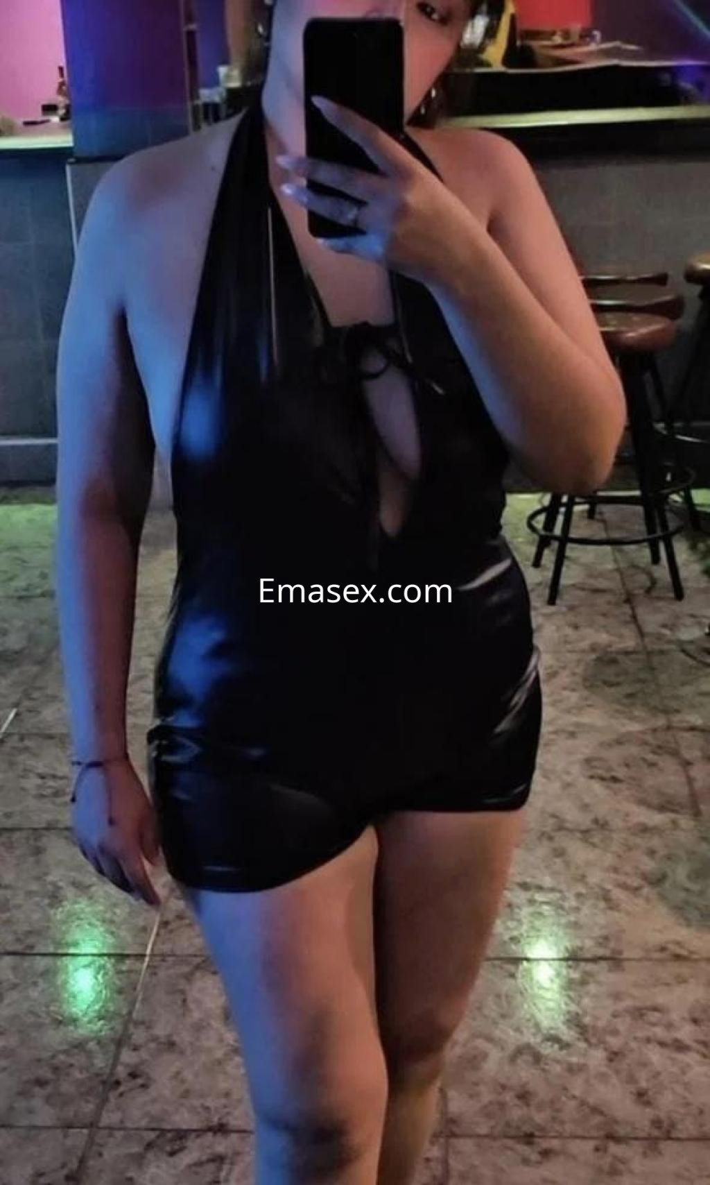 Escort en Toledo luciendo un conjunto de body negro, posando frente a un espejo en un ambiente iluminado.
