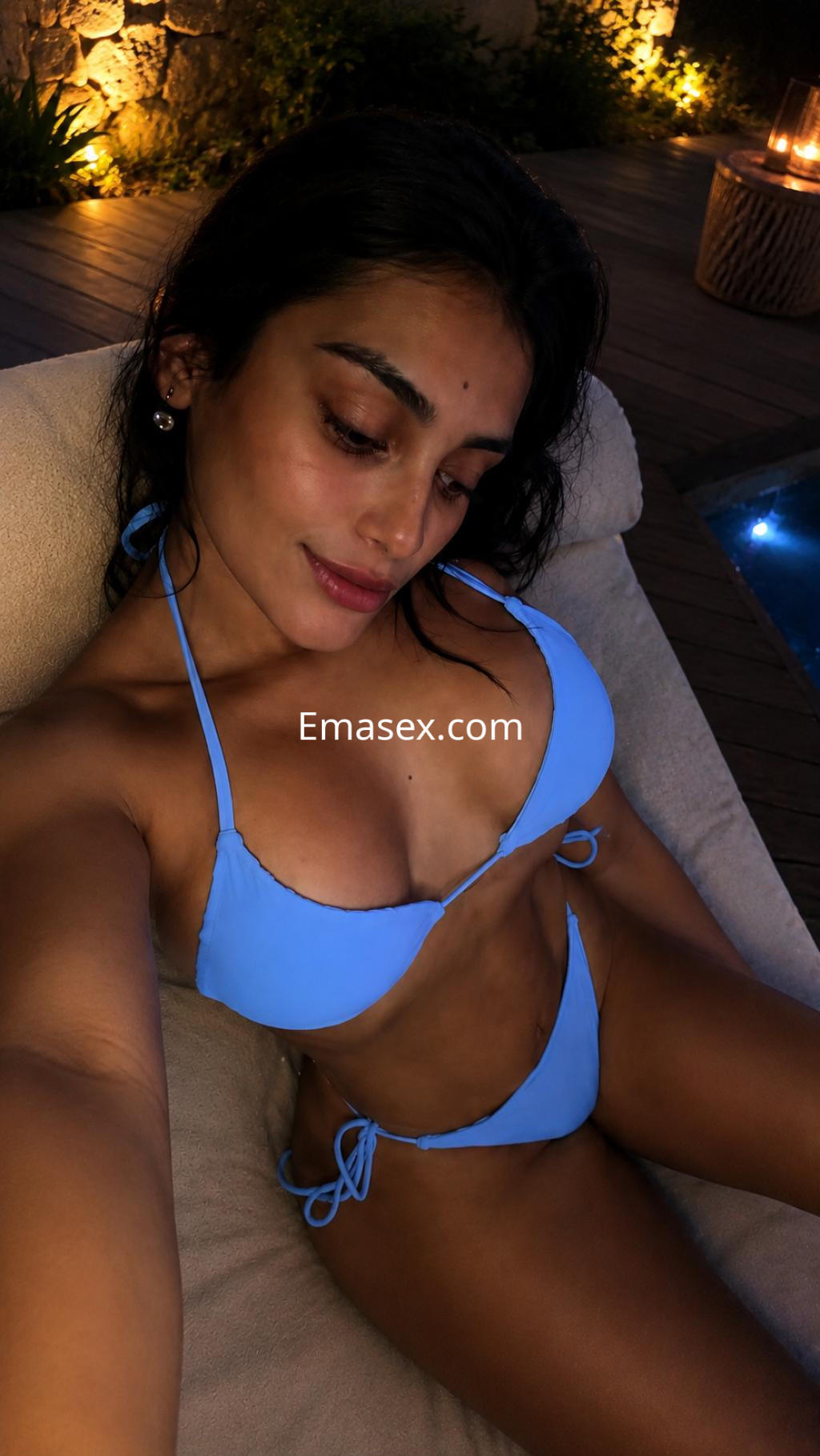Escort en Santander posando con un bikini azul en un ambiente iluminado suavemente, sentada en un sofá.
