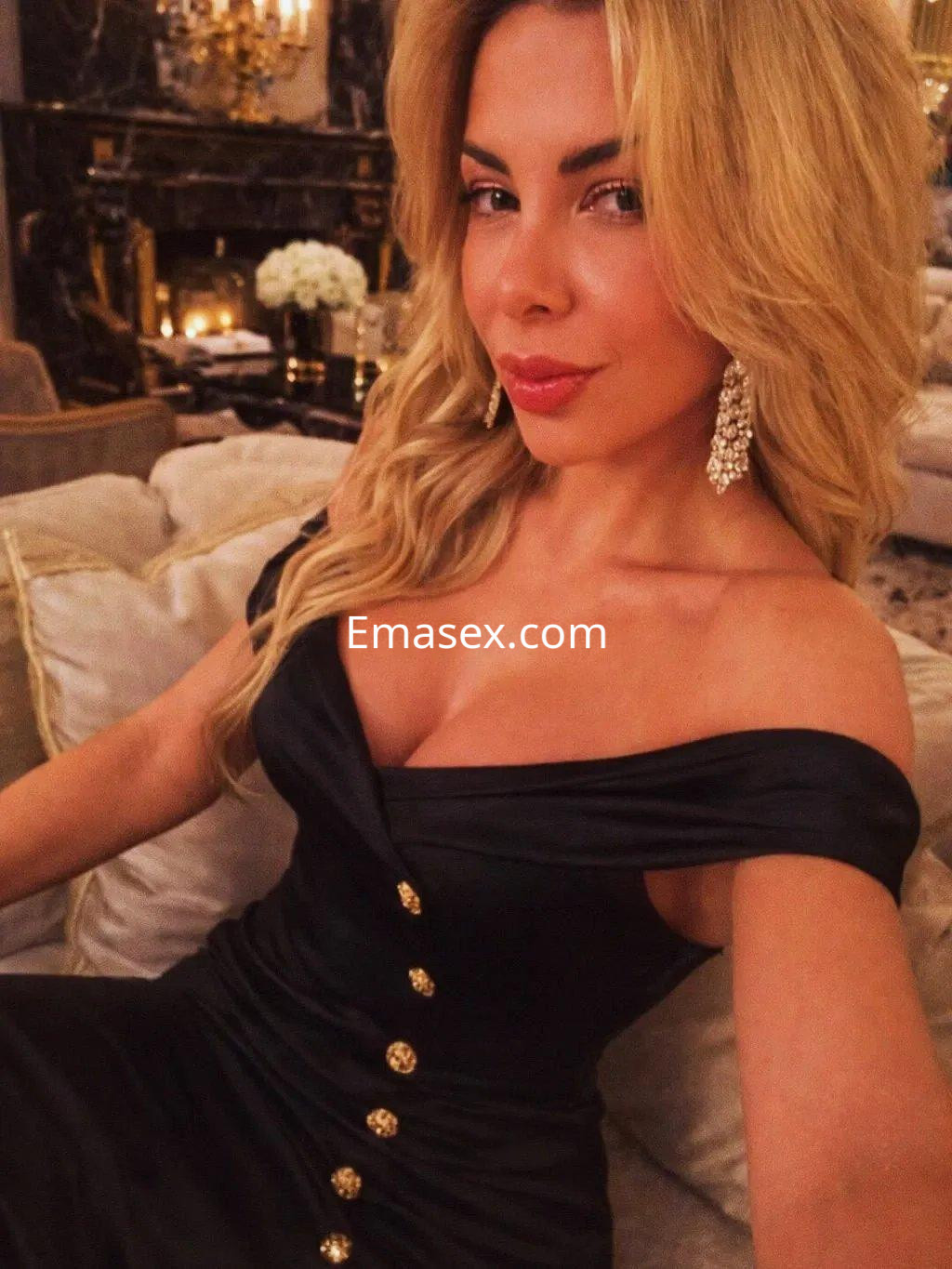 Escort en Valencia con vestido negro de escote pronunciado, cabello rubio y joyas brillantes en un elegante entorno.