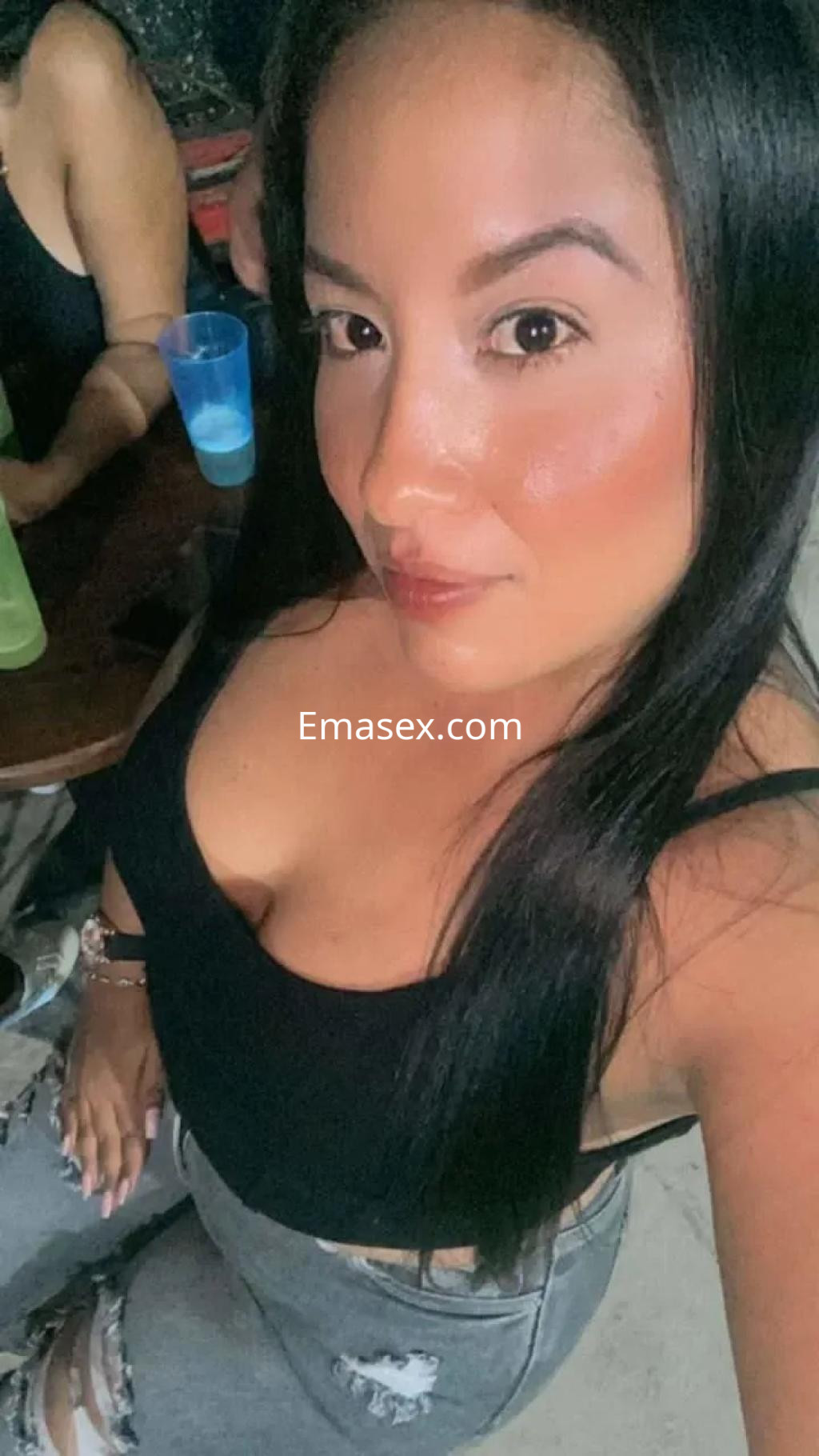 Escort con cabello largo y lacio, viste una blusa negra y jeans rotos, en un ambiente social en Granada.